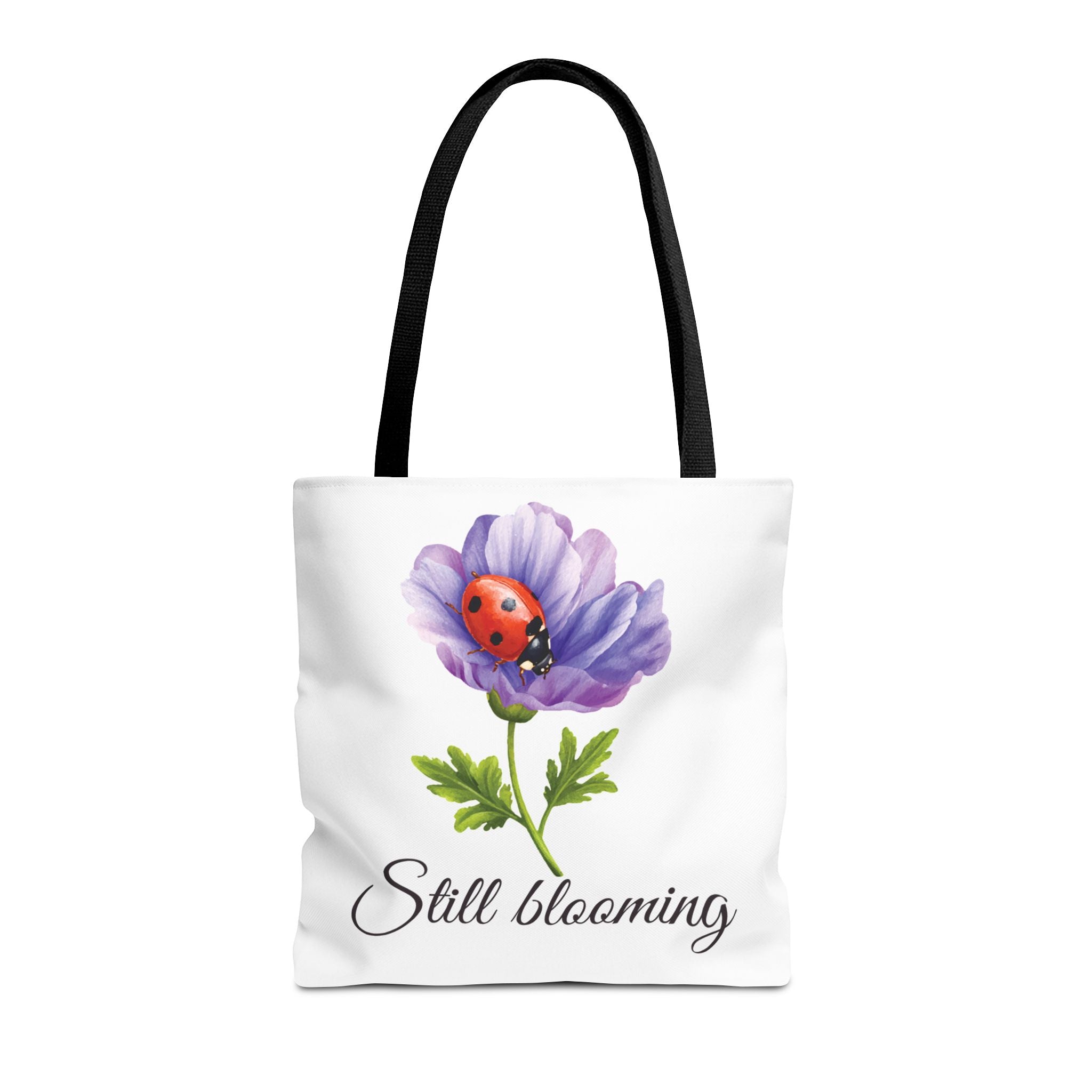 Tote bag with a purple flower and ladybug design, featuring the text 'Still Blooming'.
