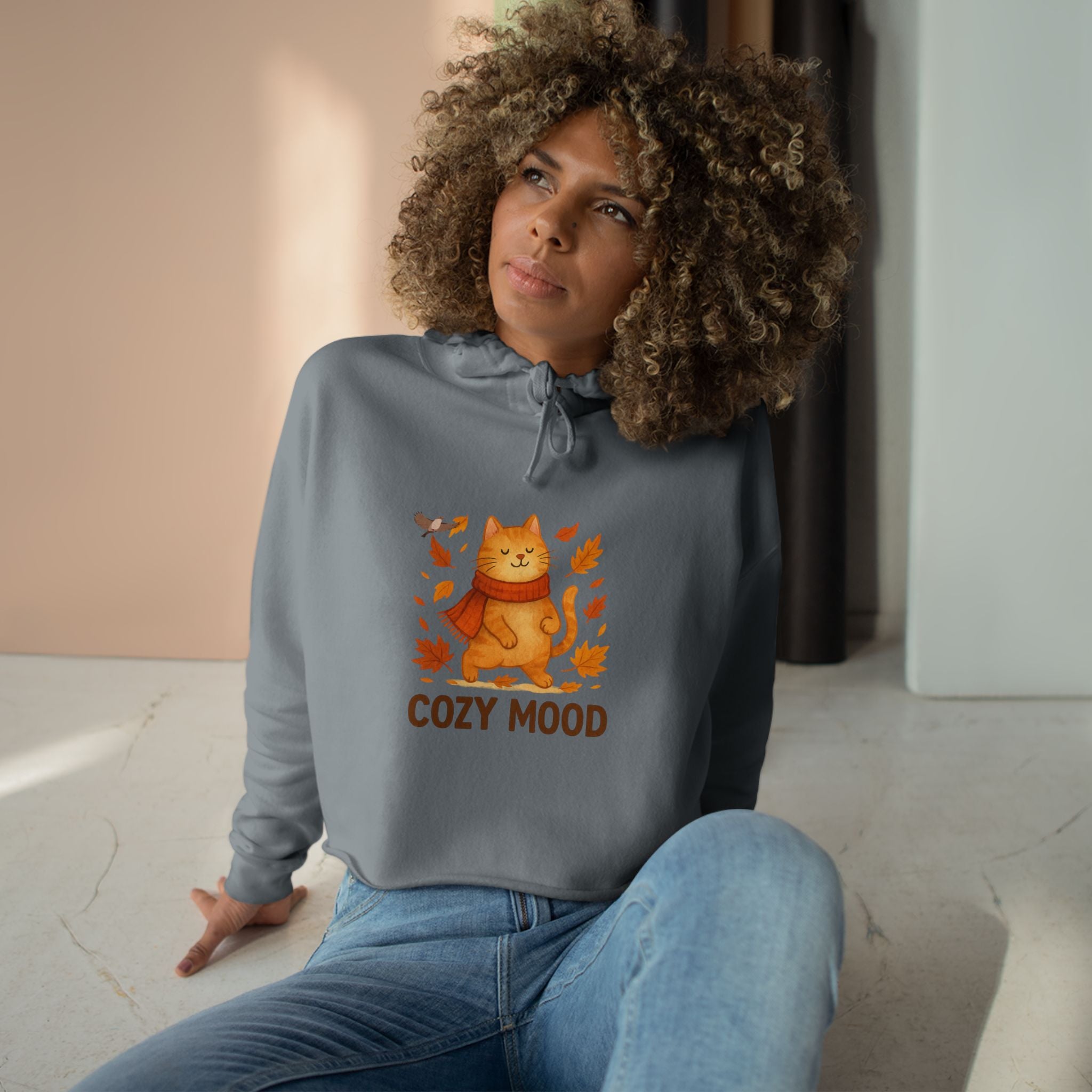 Woman wearing a gray sweatshirt with a cat graphic and 'Cozy Mood' text, sitting indoors.