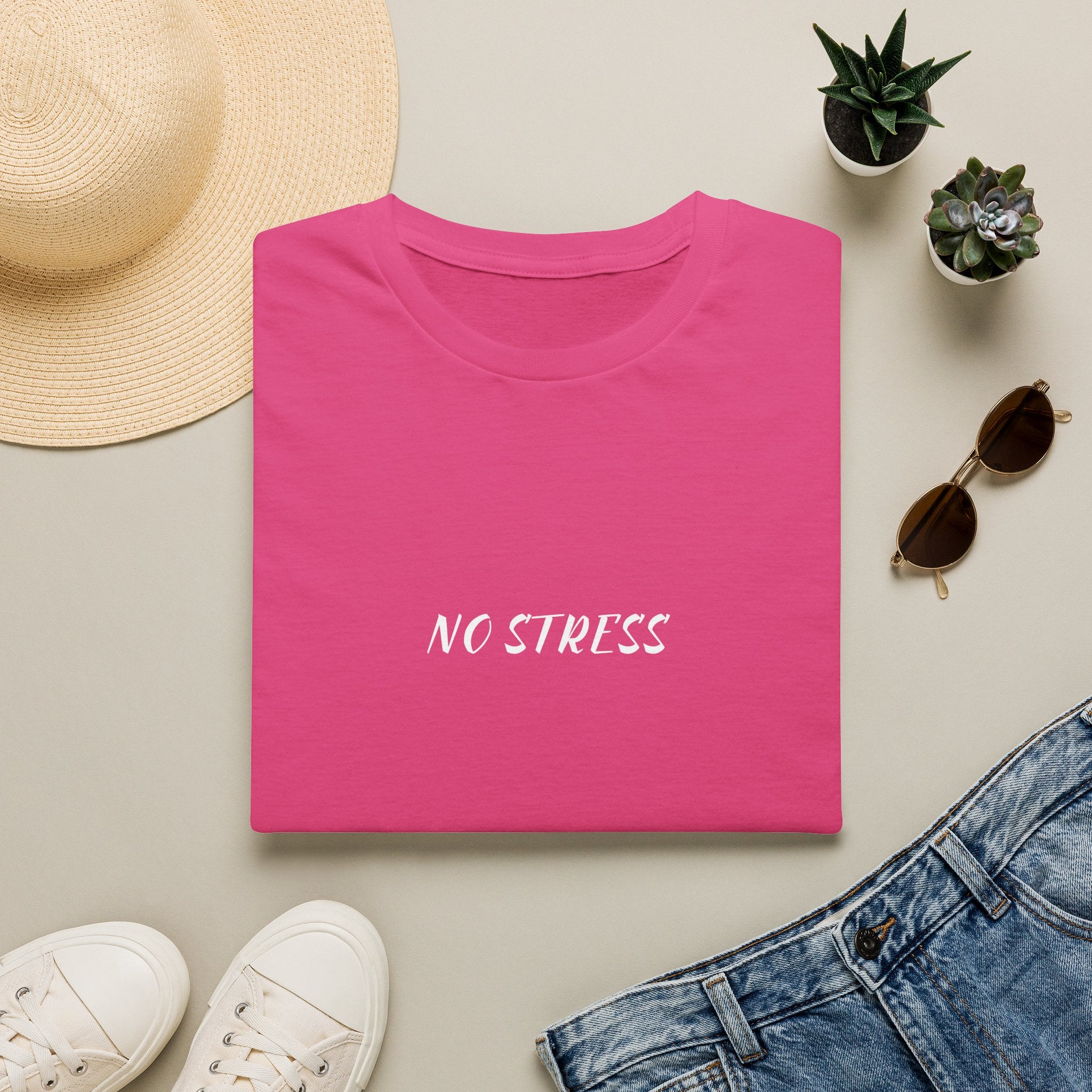 Pink t-shirt with white graphic design and text 'POISON' on a beige surface with casual items.