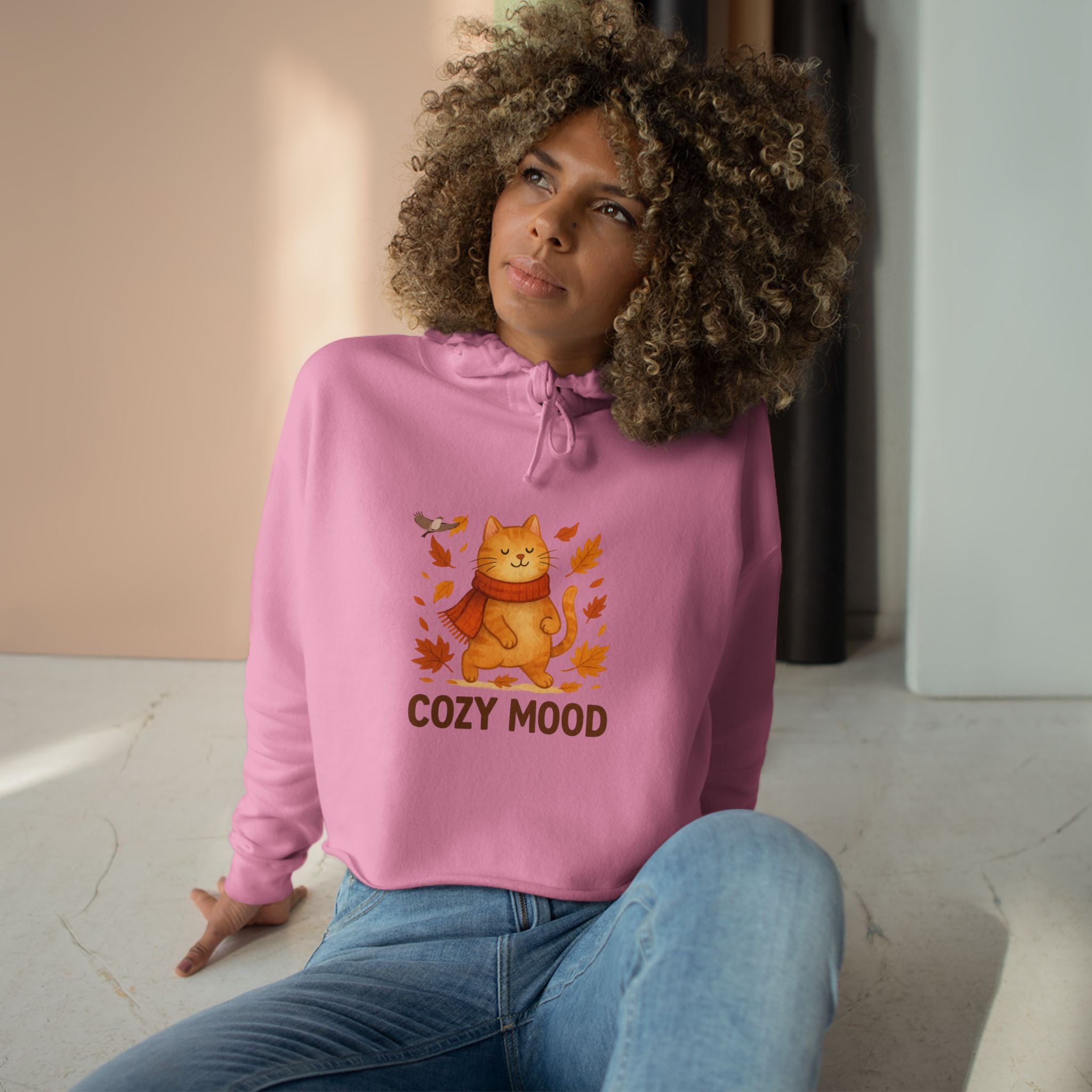 Woman wearing a pink hoodie with a cat graphic and 'Cozy Mood' text, sitting indoors.