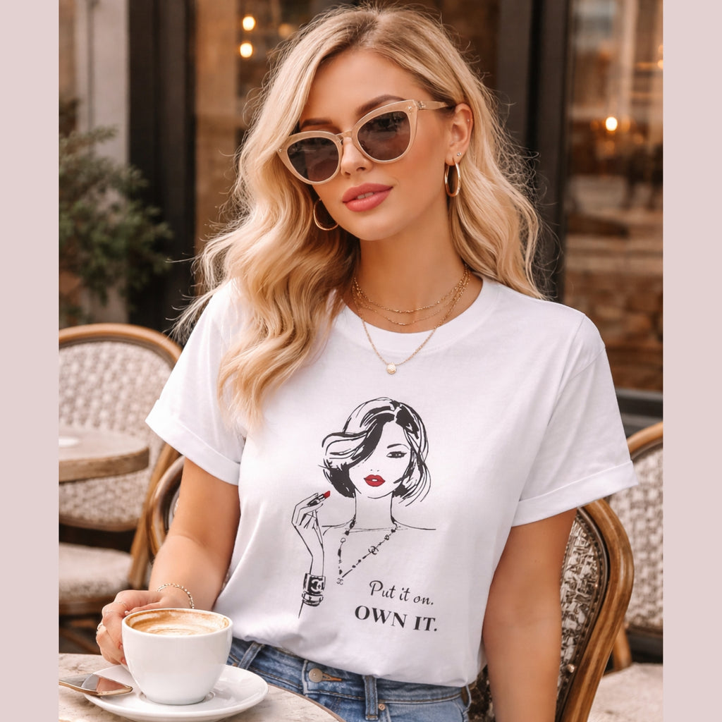 Woman wearing a white t-shirt with a graphic design, sitting at an outdoor cafe.
