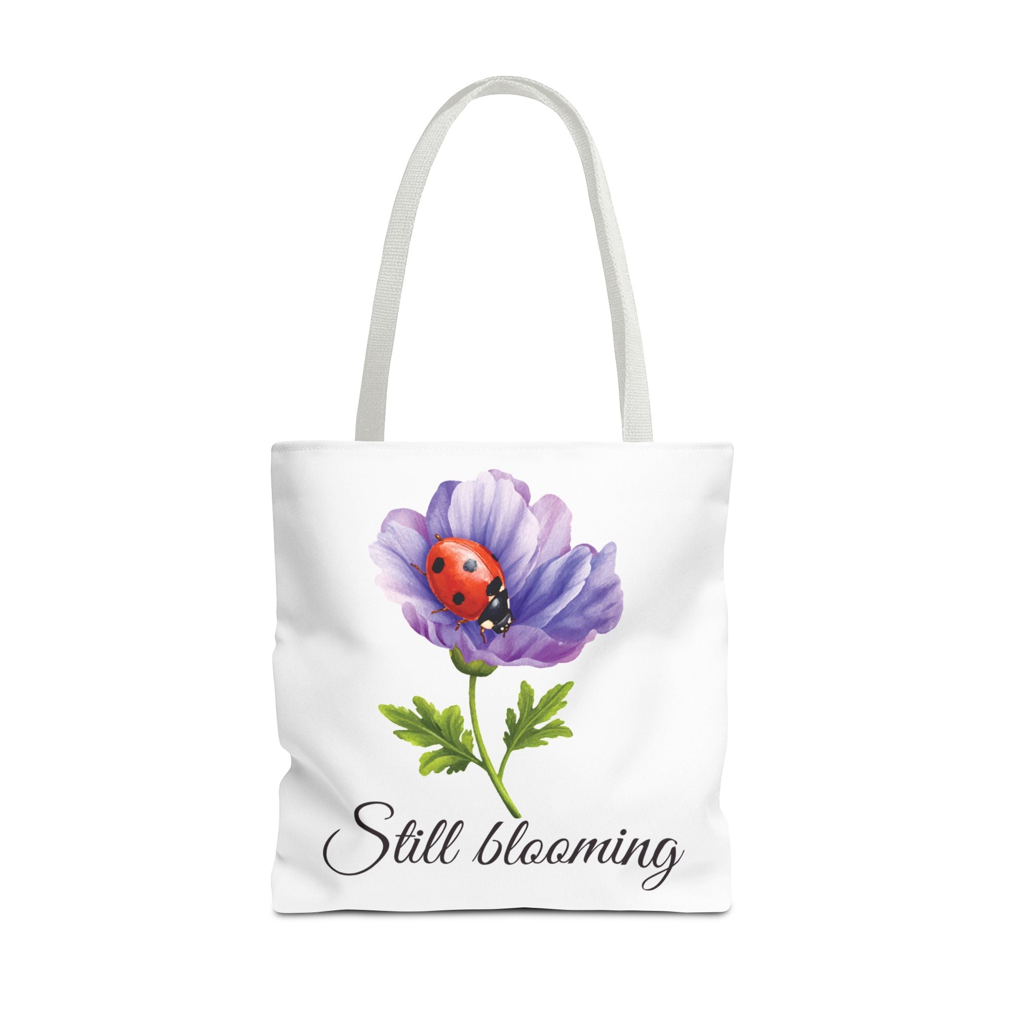 Tote bag with a purple flower and ladybug design, featuring the text 'Still blooming'.