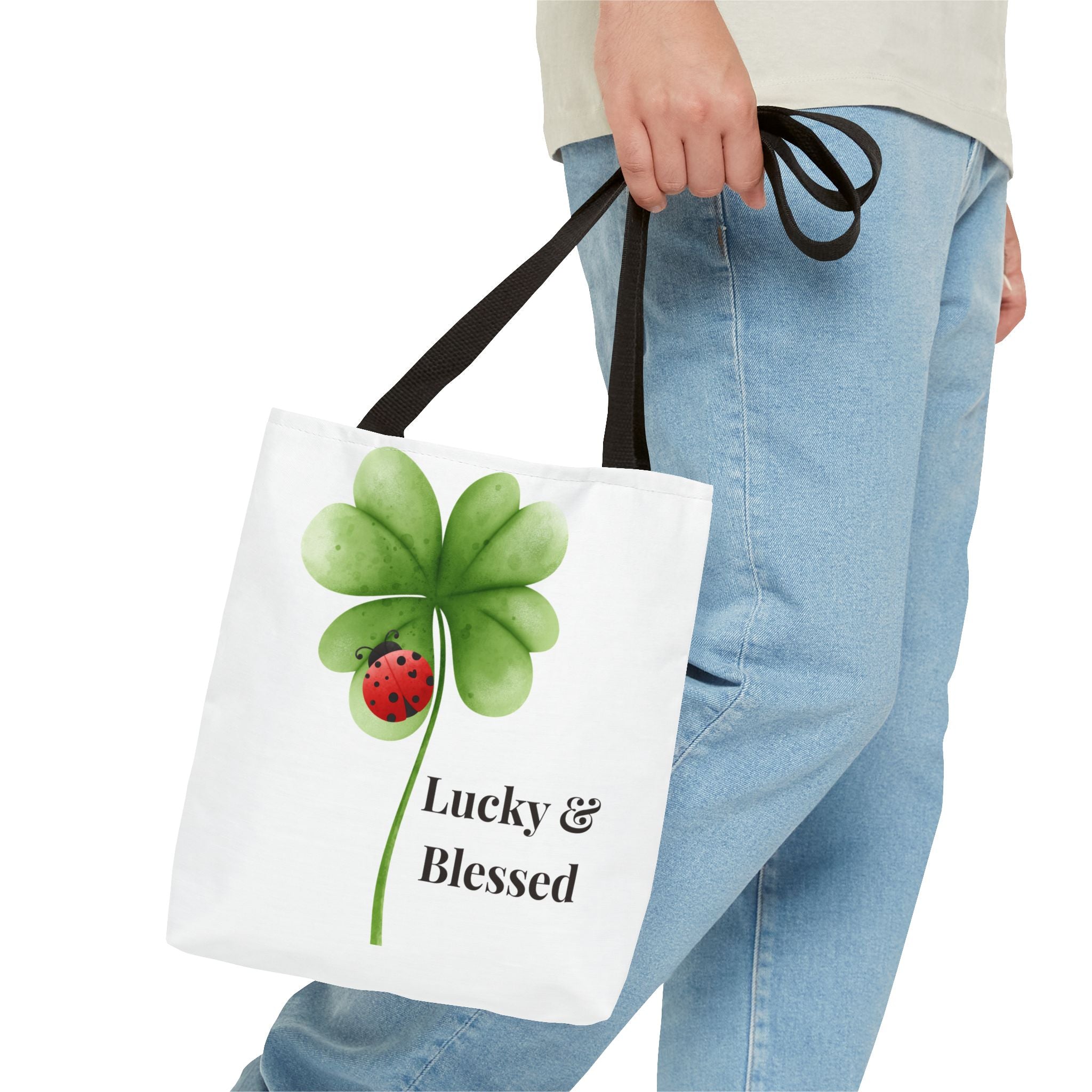 Tote bag with a four-leaf clover and ladybug design, held by a person wearing jeans.