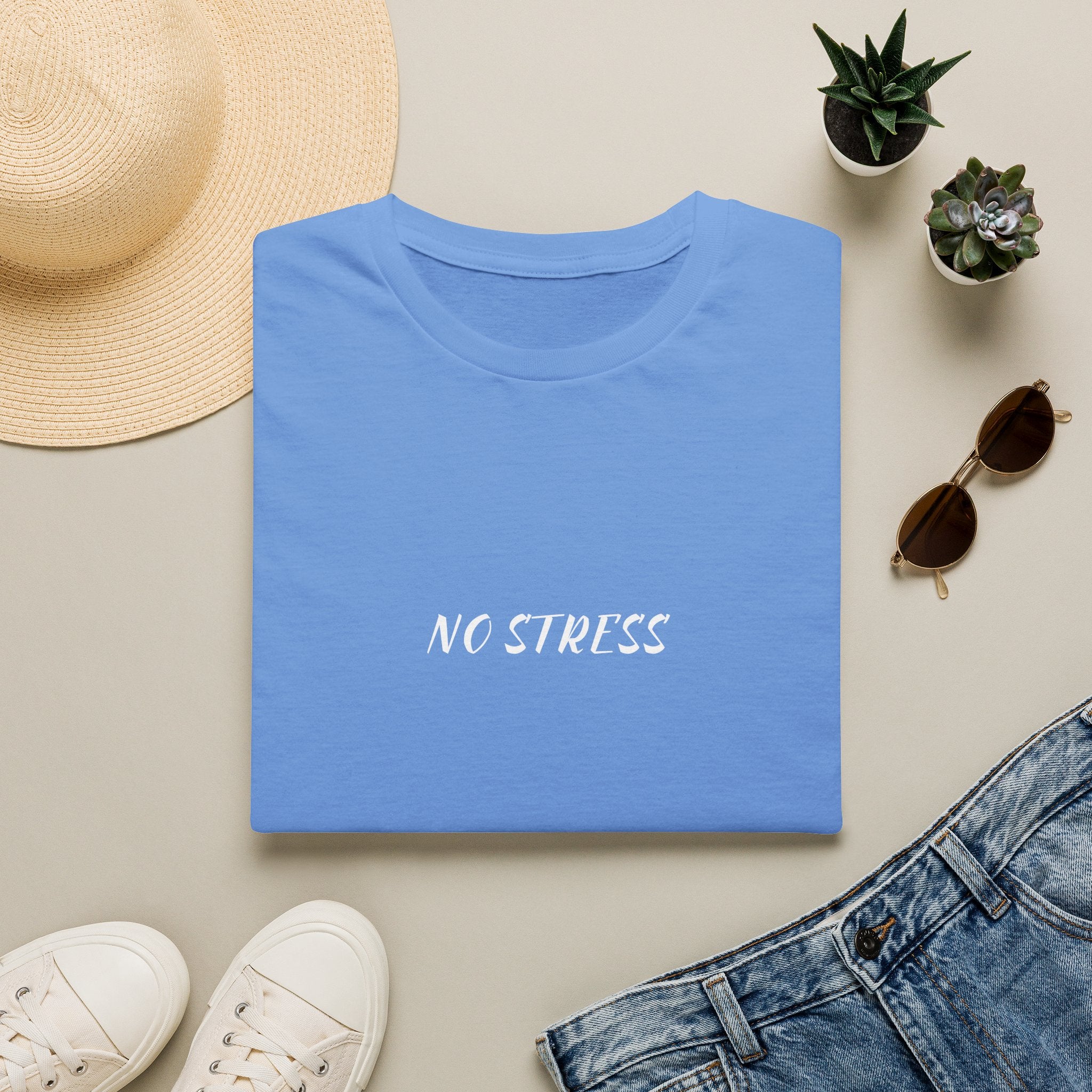 Folded blue t-shirt with 'NO STRESS' text on a beige surface with casual items.