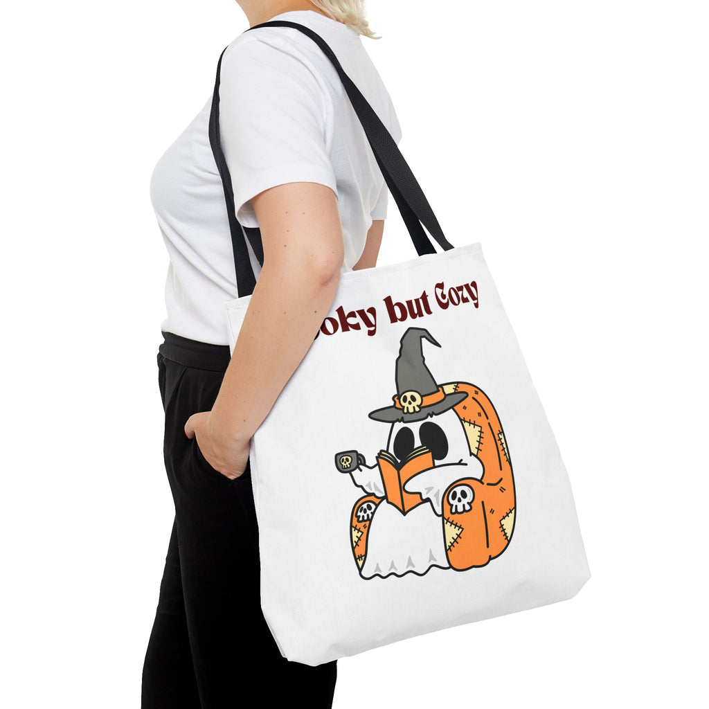 Person holding a white tote bag with a Halloween-themed design and text.