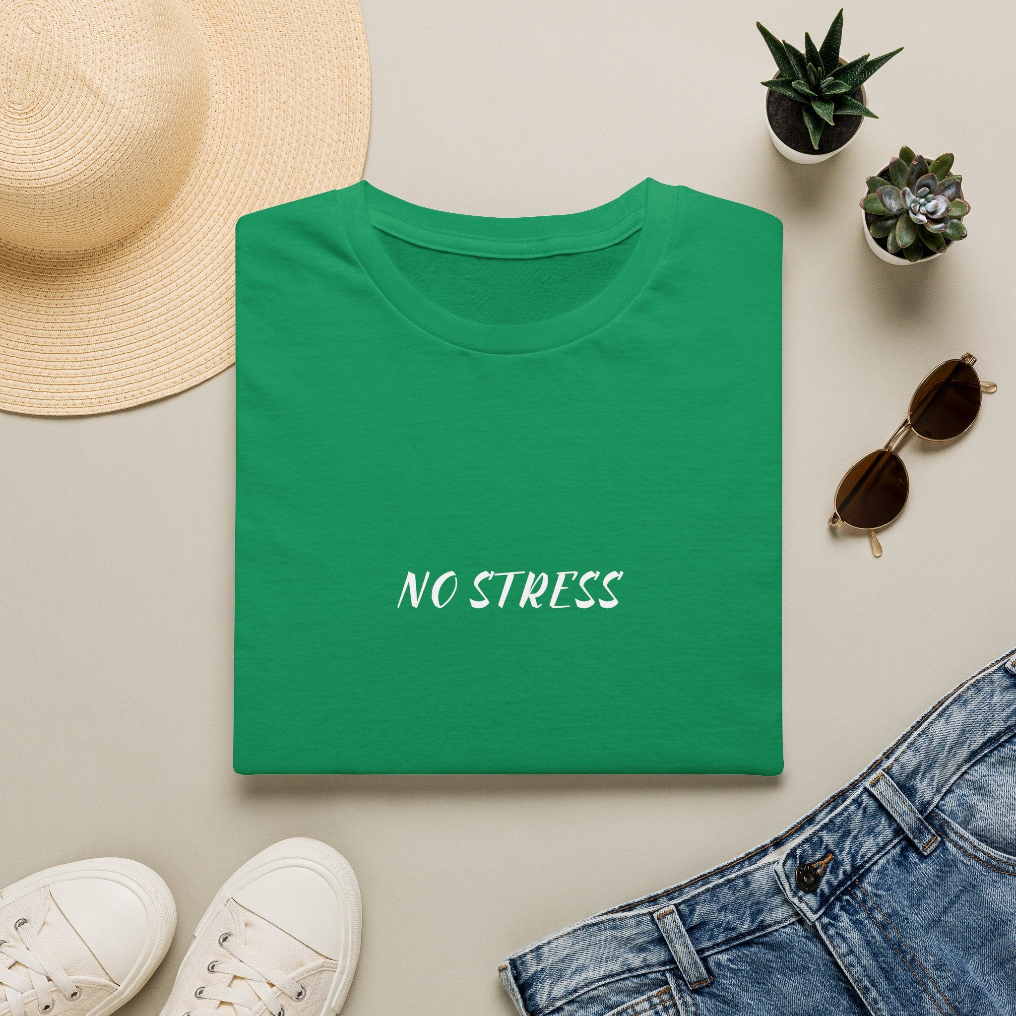 Green t-shirt with 'NO STRESS' text on a light surface with casual items like a hat, sunglasses, and shoes.