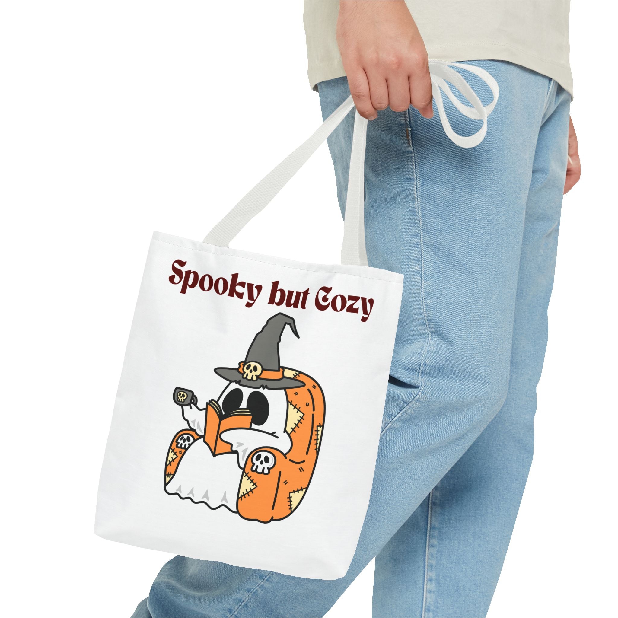 Tote bag with Halloween design and text 'Spooky but Cozy' held by a person wearing jeans.