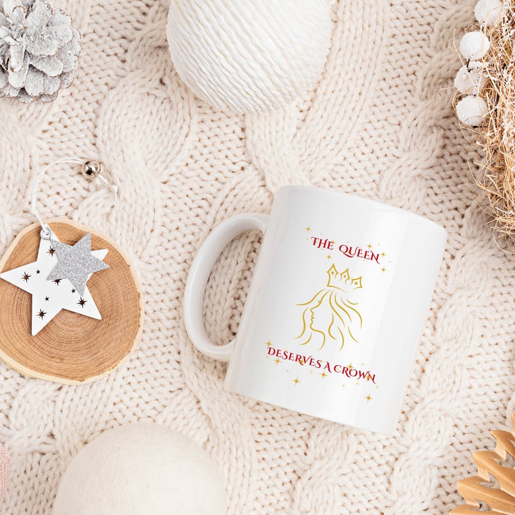 White mug with 'The Queen Deserves a Crown' text on a textured beige surface.