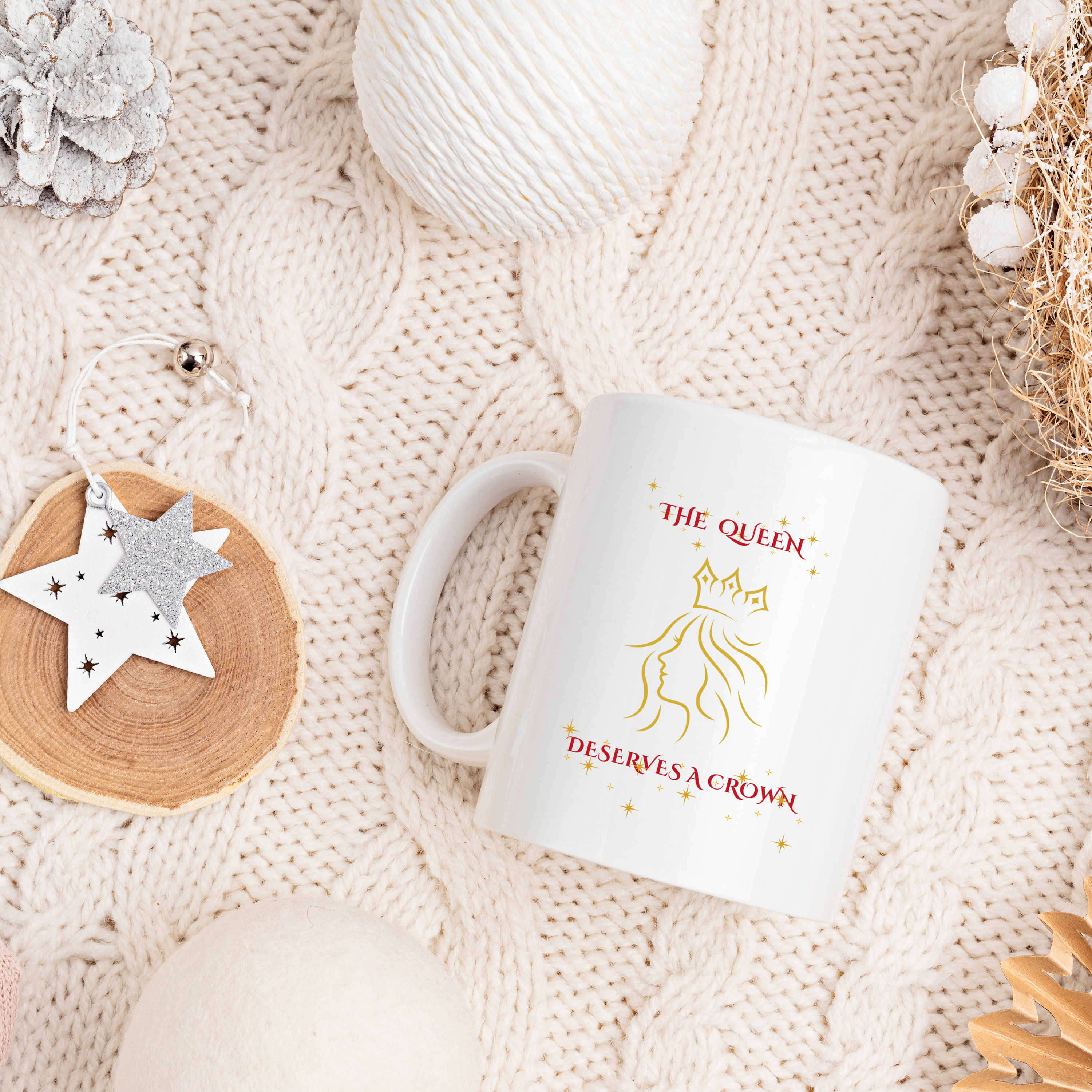White mug with 'The Queen Deserves a Crown' text on a textured beige surface.