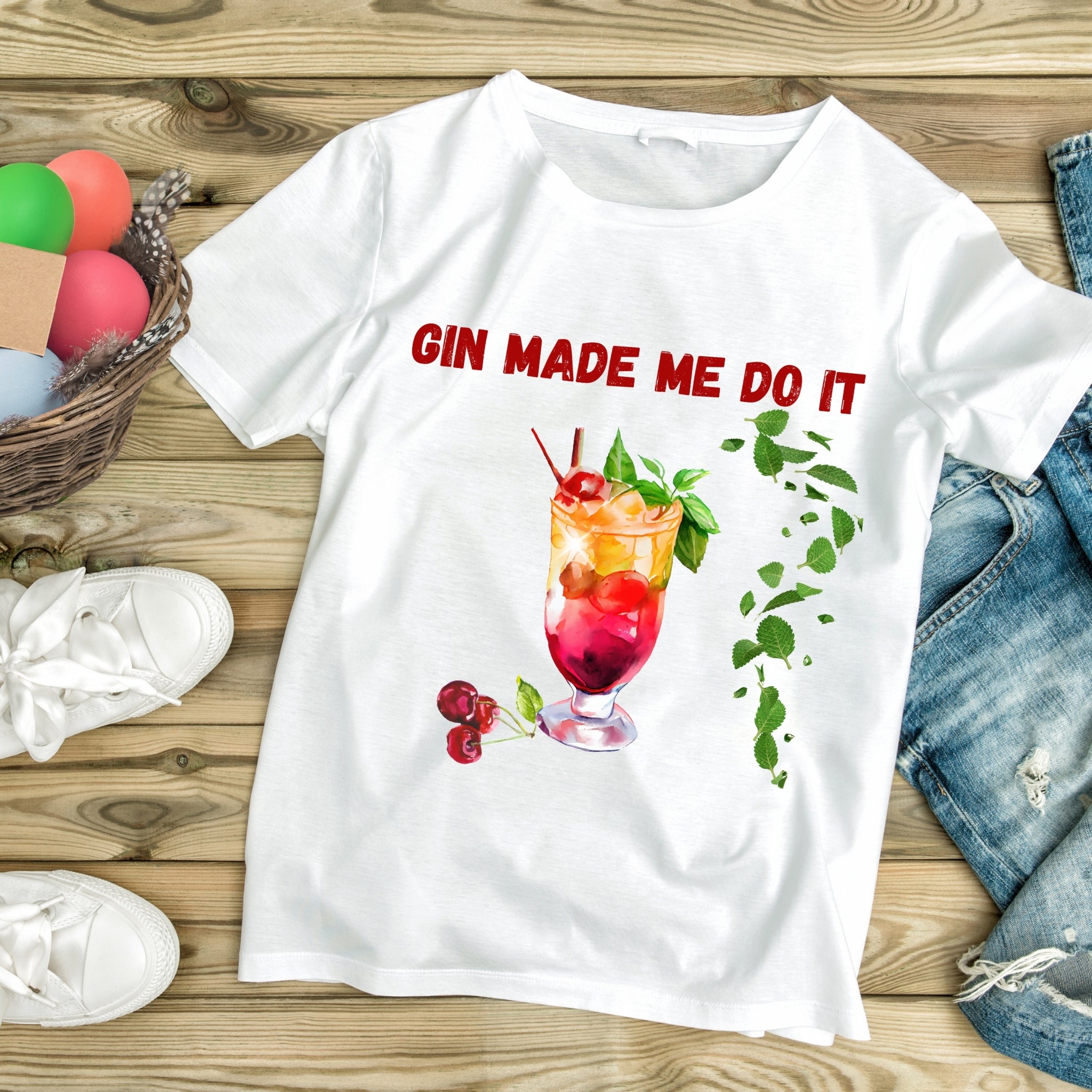 White t-shirt with 'Gin Made Me Do It' graphic on a wooden surface with casual items.