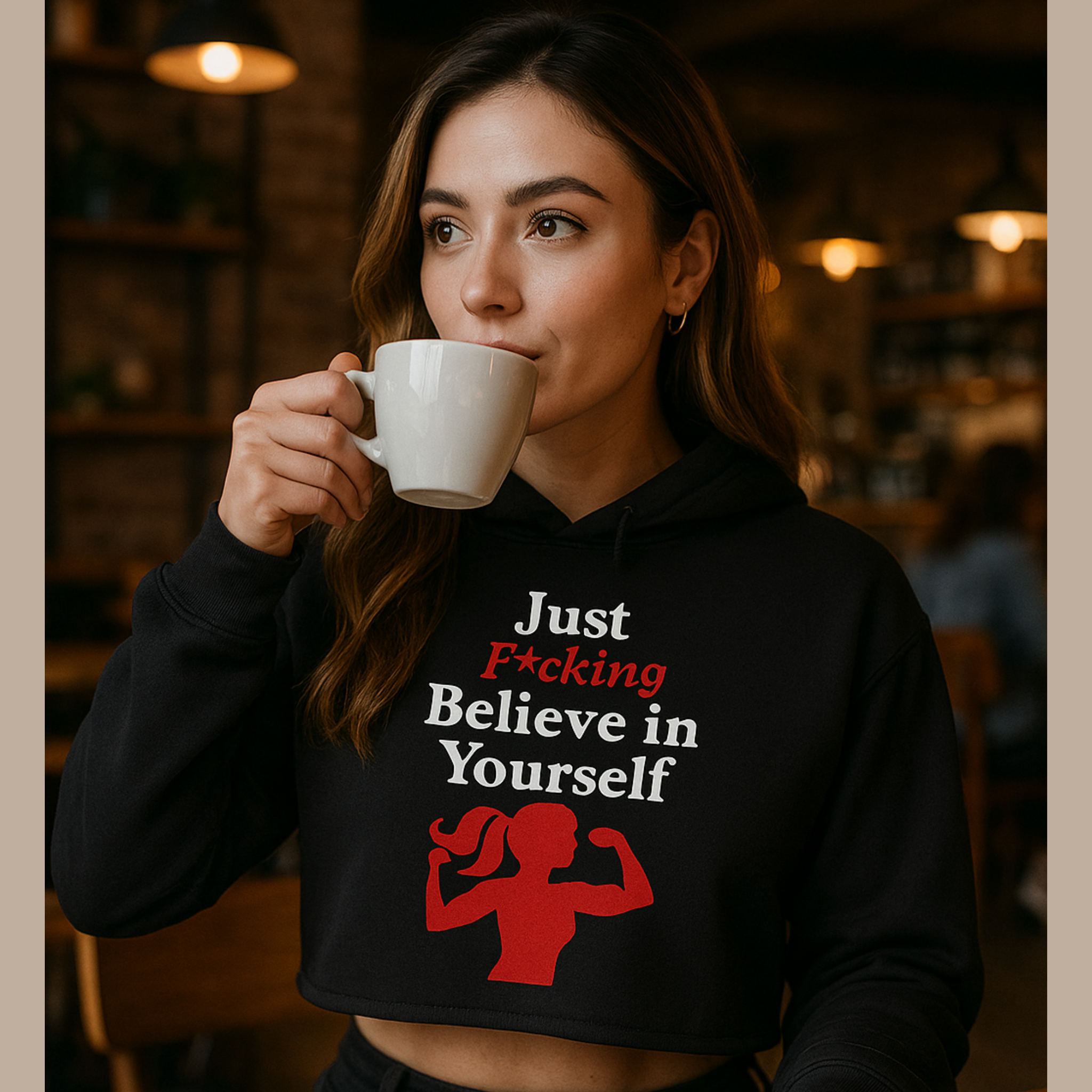 Woman wearing a black hoodie with motivational text and graphic, drinking from a white mug in a cozy setting.